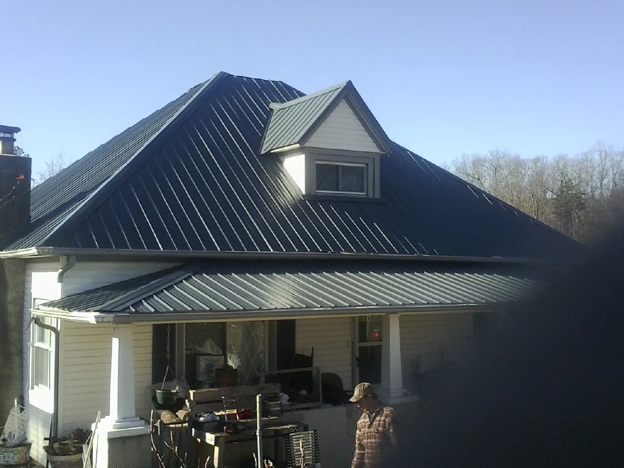 Dark blue standing seam metal roof with a dormer above a front porch in Ames