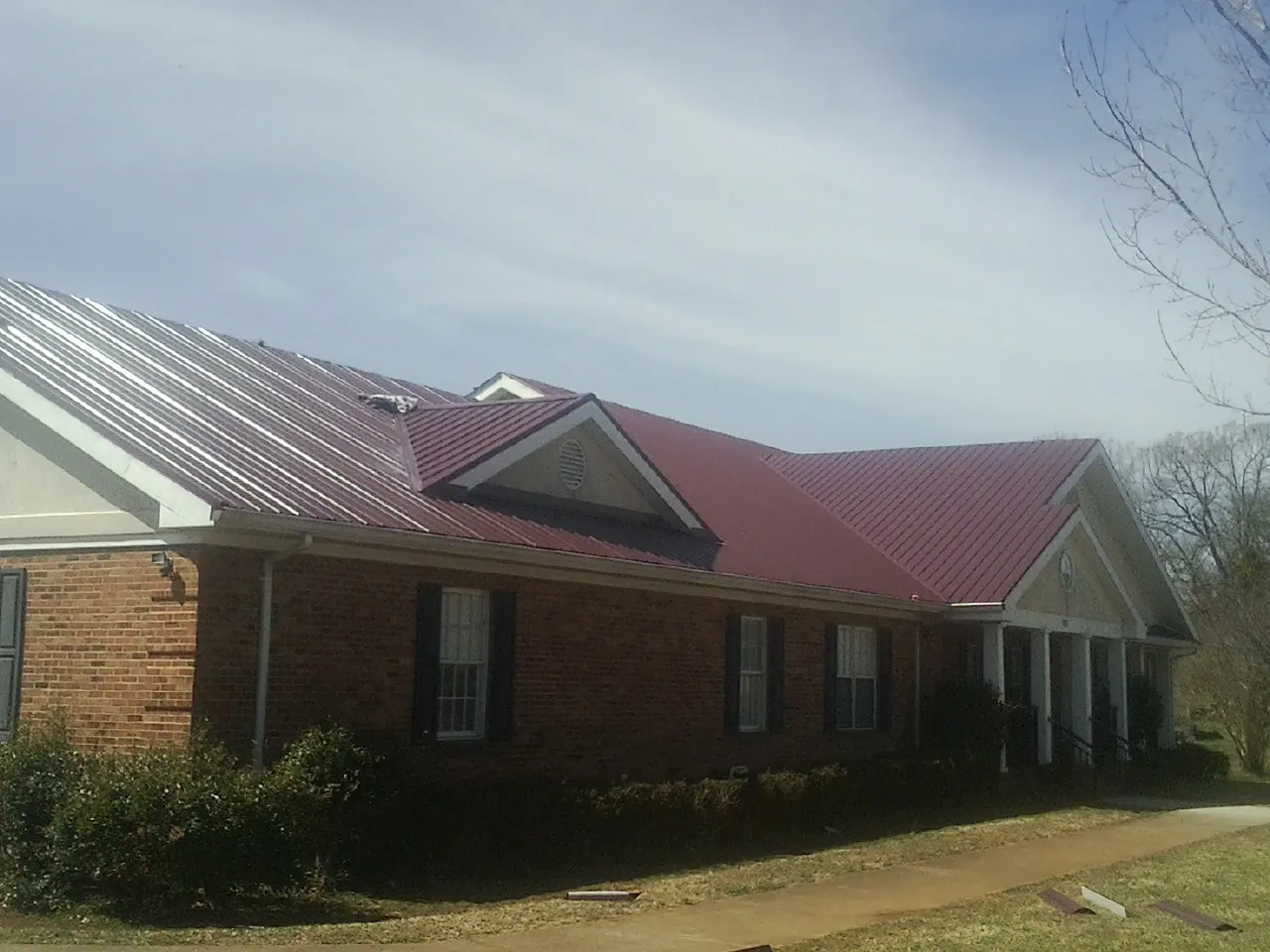 Red metal roof with gabled entries on a long brick building, from a Hail Damage Roof Repair job in Ames