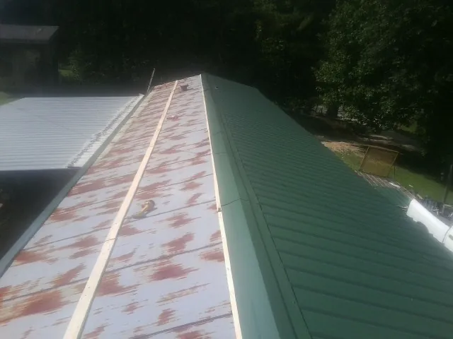 Old rusted panels beside newly installed green metal roofing — Wind Damage Roof Repair by Roofing Brothers in Ames