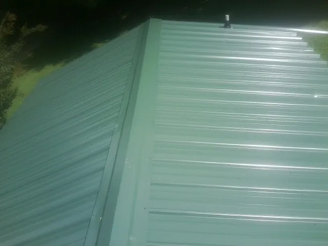 New green metal panels meeting at the ridge of a roof — Flat Roof Repair work by our crew in Ames
