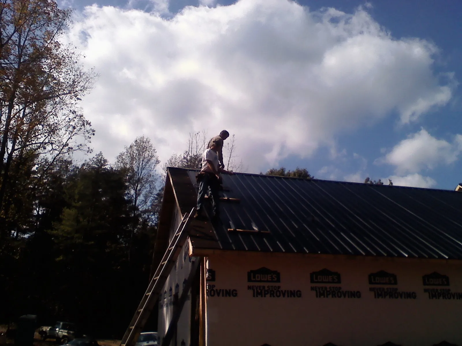 Roofer fastening dark metal panels high against a cloudy sky, from a Roof Inspection job in Ames